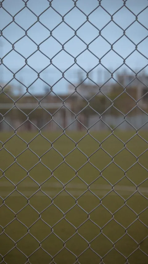 Close-up of a chain-link fence pattern at an outdoor sports field with blurred background.