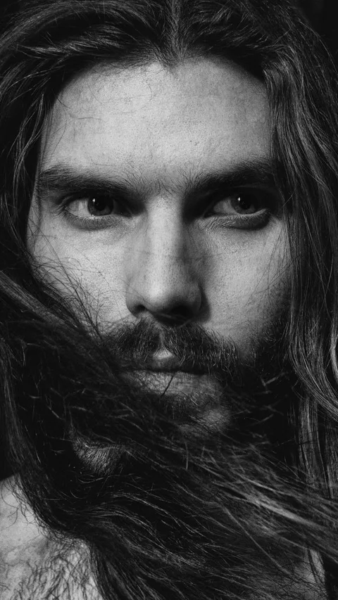 Intense close-up black and white portrait of a bearded man with long hair.