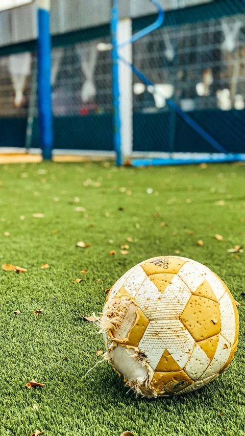 A worn-out soccer ball lies on an unkempt field, symbolizing forgotten play.