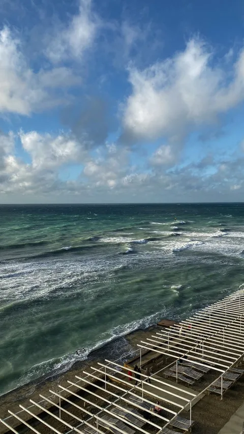 A stunning aerial shot of the Black Sea waves breaking on Anapa beach, Russia under a partly cloudy sky.