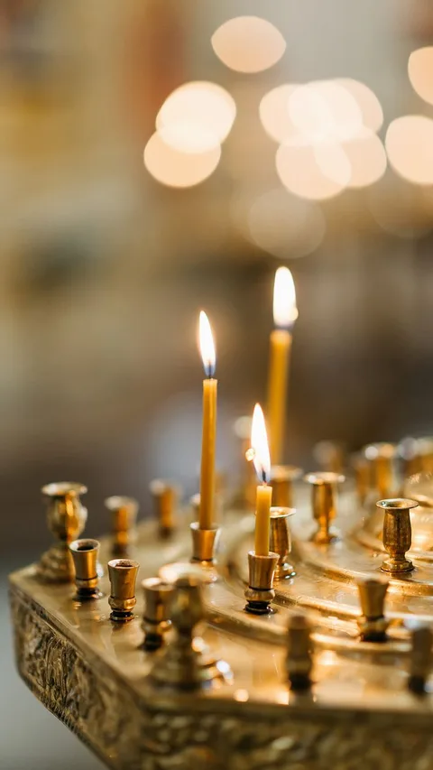 Close-up of a golden candlestick with lit taper candles in a dimly lit setting.