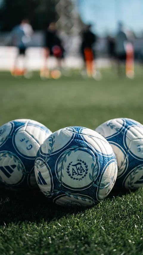 Close-up of soccer balls on a grass field with players in the background.