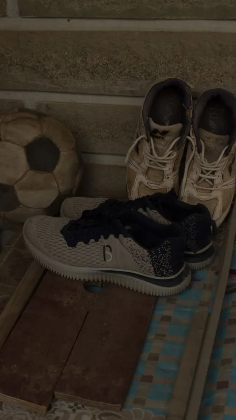 A pair of sneakers and a football against a stone wall in Bengaluru, India.