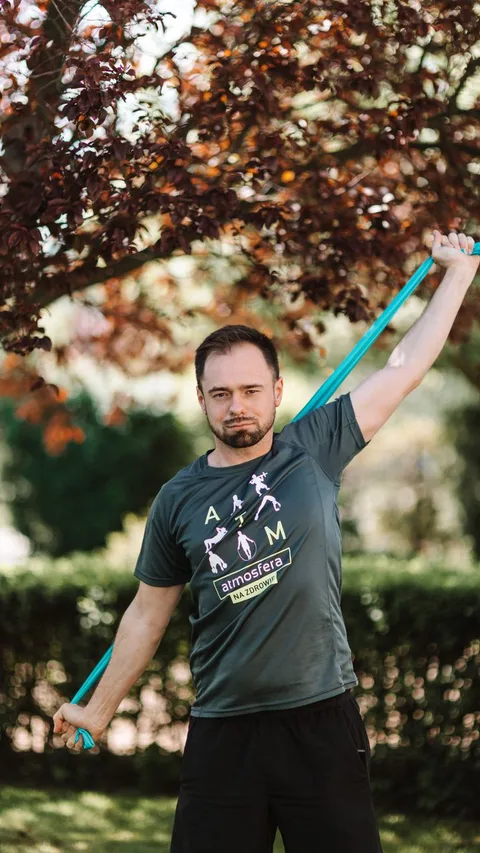 Adult male exercising with a resistance band outdoors in a park setting, promoting wellness and fitness.