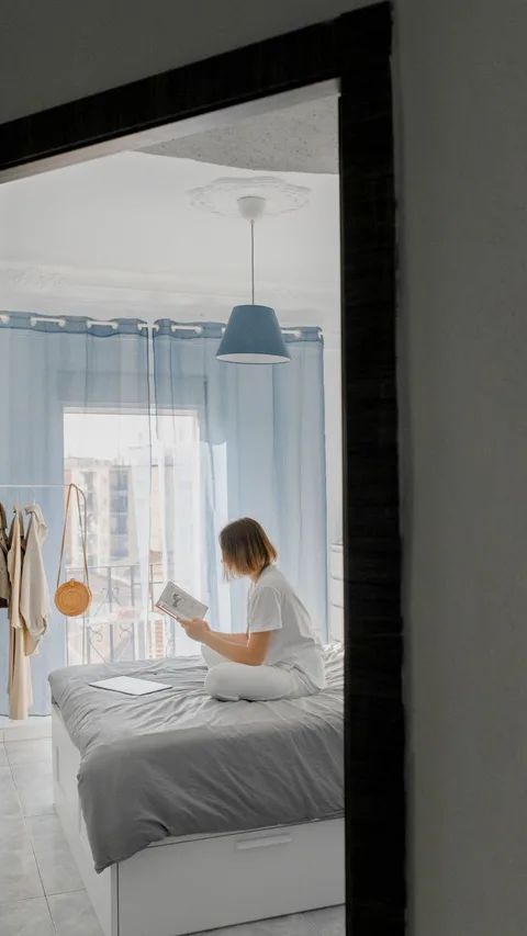 Woman relaxing and reading in a serene, modern bedroom with soft light and blue accents.
