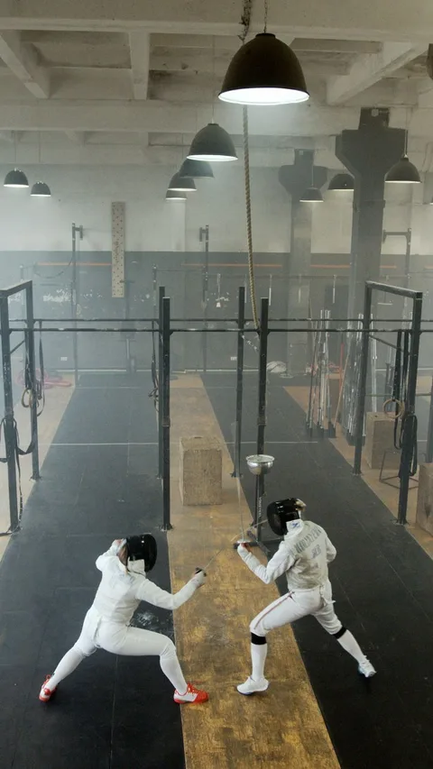 Two fencers in action during a practice session in an indoor gym.