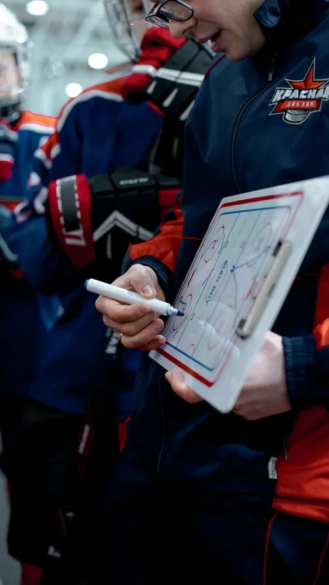 Ice hockey coach explaining strategy to players on a whiteboard.