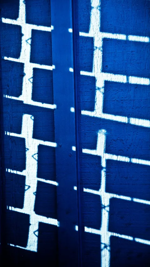 Vertical abstract shadows forming patterns on a textured blue wall.