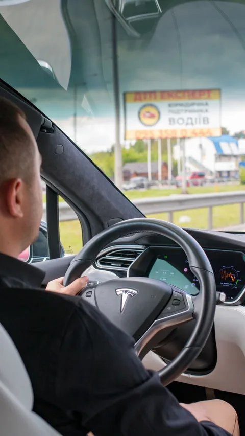 A man drives a Tesla Model S, capturing the modern driving experience in a city setting.